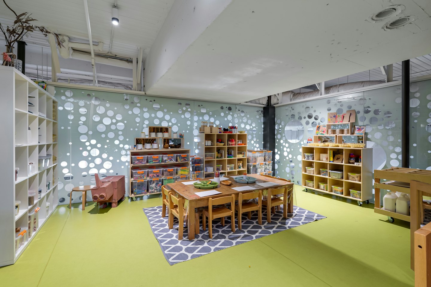 Children's art room with wooden tables and craft supplies on shelves.