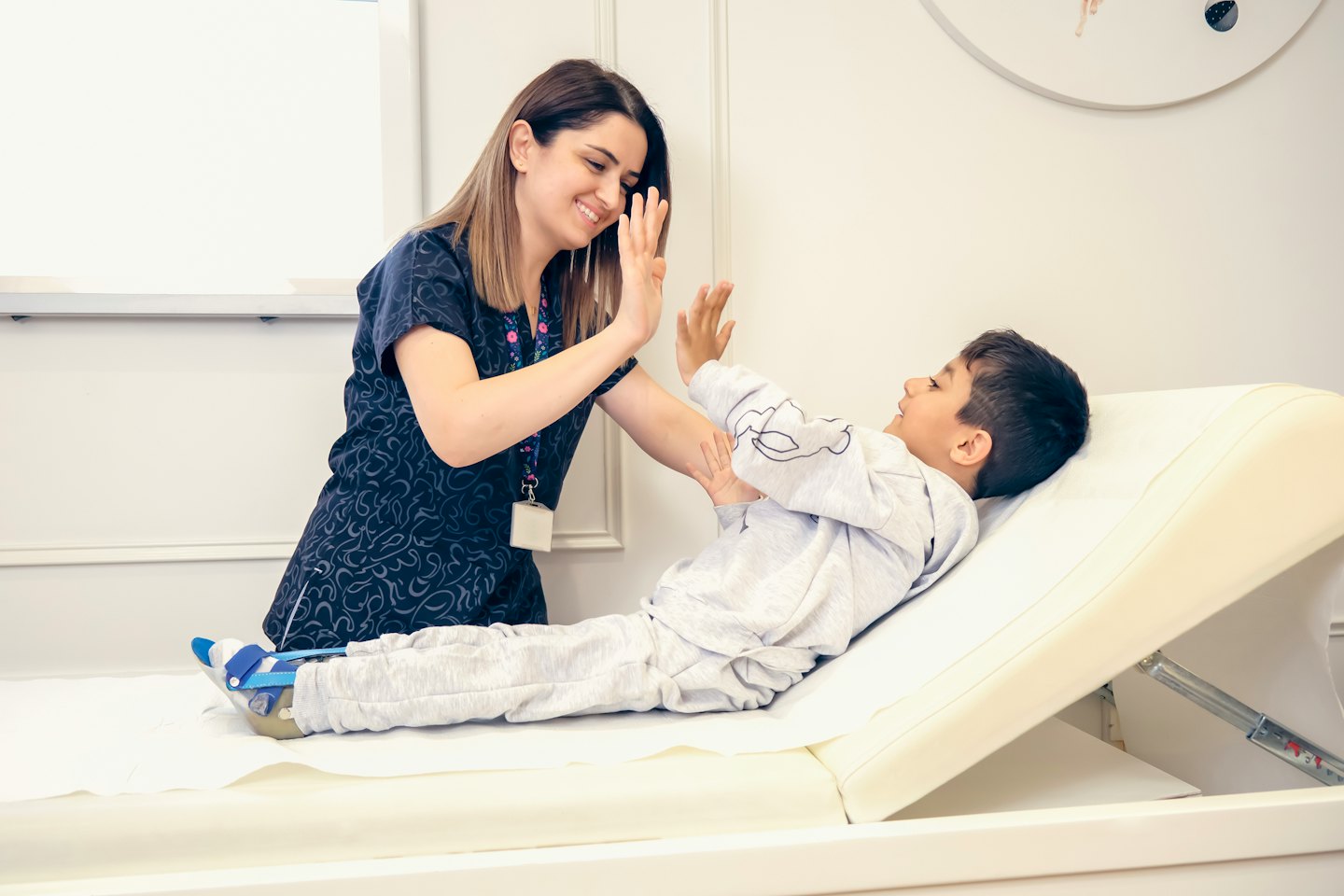 Woman gives a boy with a leg brace a high-five on an exam table.